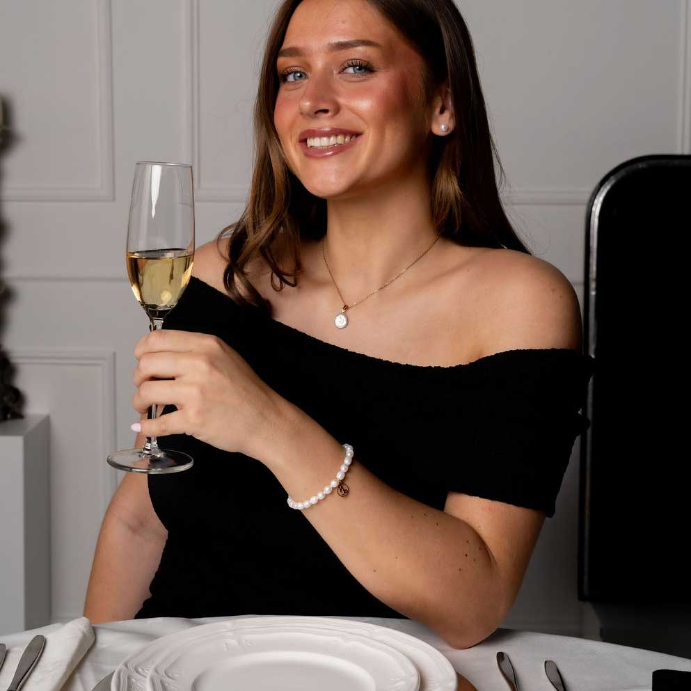 Wit parel armband met gouden edelstalen symbool sterrenbeeld steenbok op model aan tafel | Parel armband Gouden Sterrenbeeld Steenbok