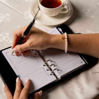 Wit parel armband met gouden edelstalen symbool sterrenbeeld steenbok op model met agenda | Parel armband Gouden Sterrenbeeld Steenbok