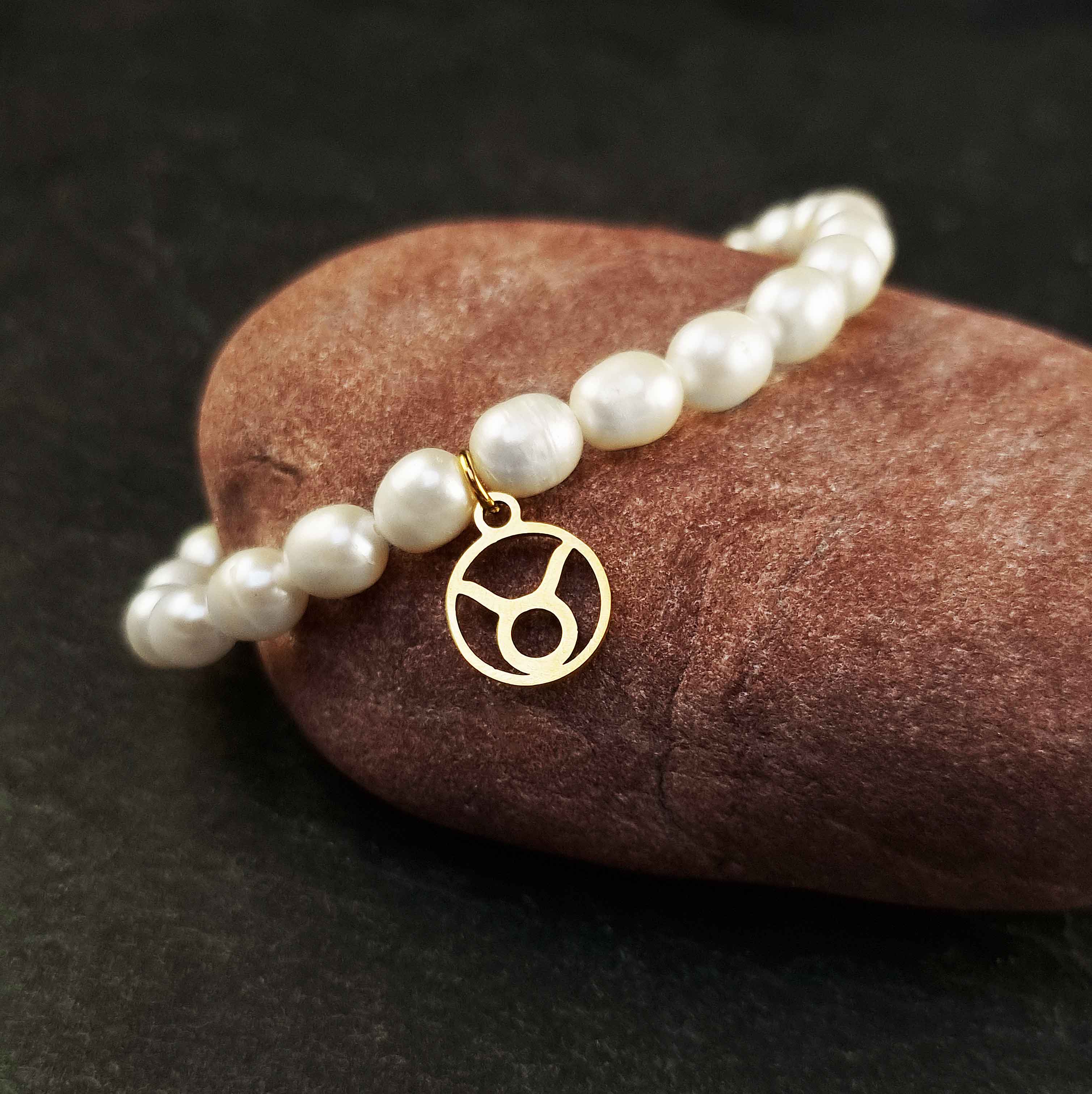 Wit zoetwater parel armband met goud edelstalen bedeltje van sterrenbeeld Stier liggend op rode steen | Gouden Sterrenbeeld Stier