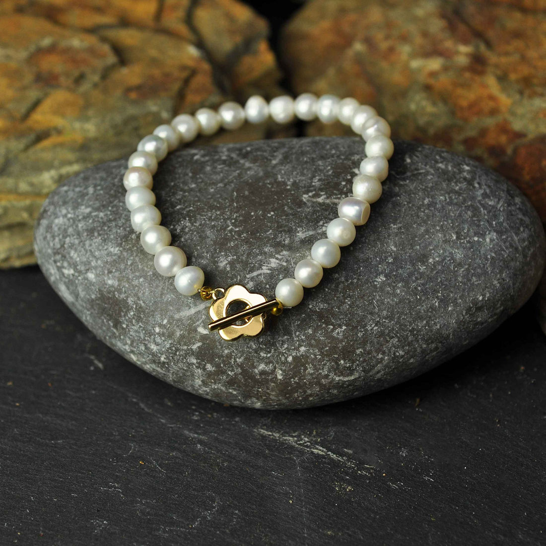 Wit zoetwater parel armband met gouden bloem slotje liggend op kei | Pearl Golden Flower