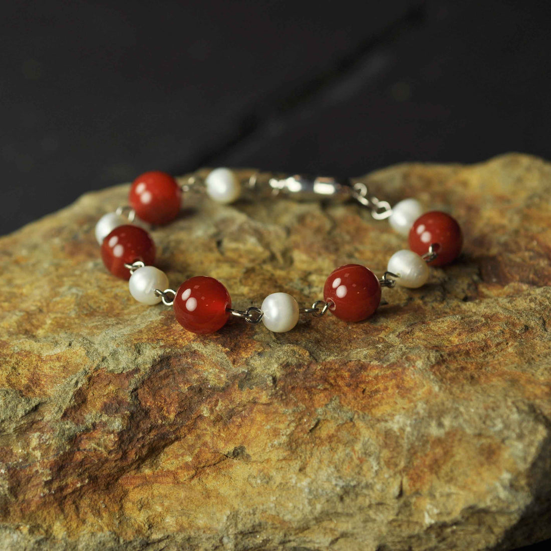 Wit zoetwater parel armband met rode edelstenen (agaat) en magneetslotje liggend op oranje steen - Pearl Red Agate Ball