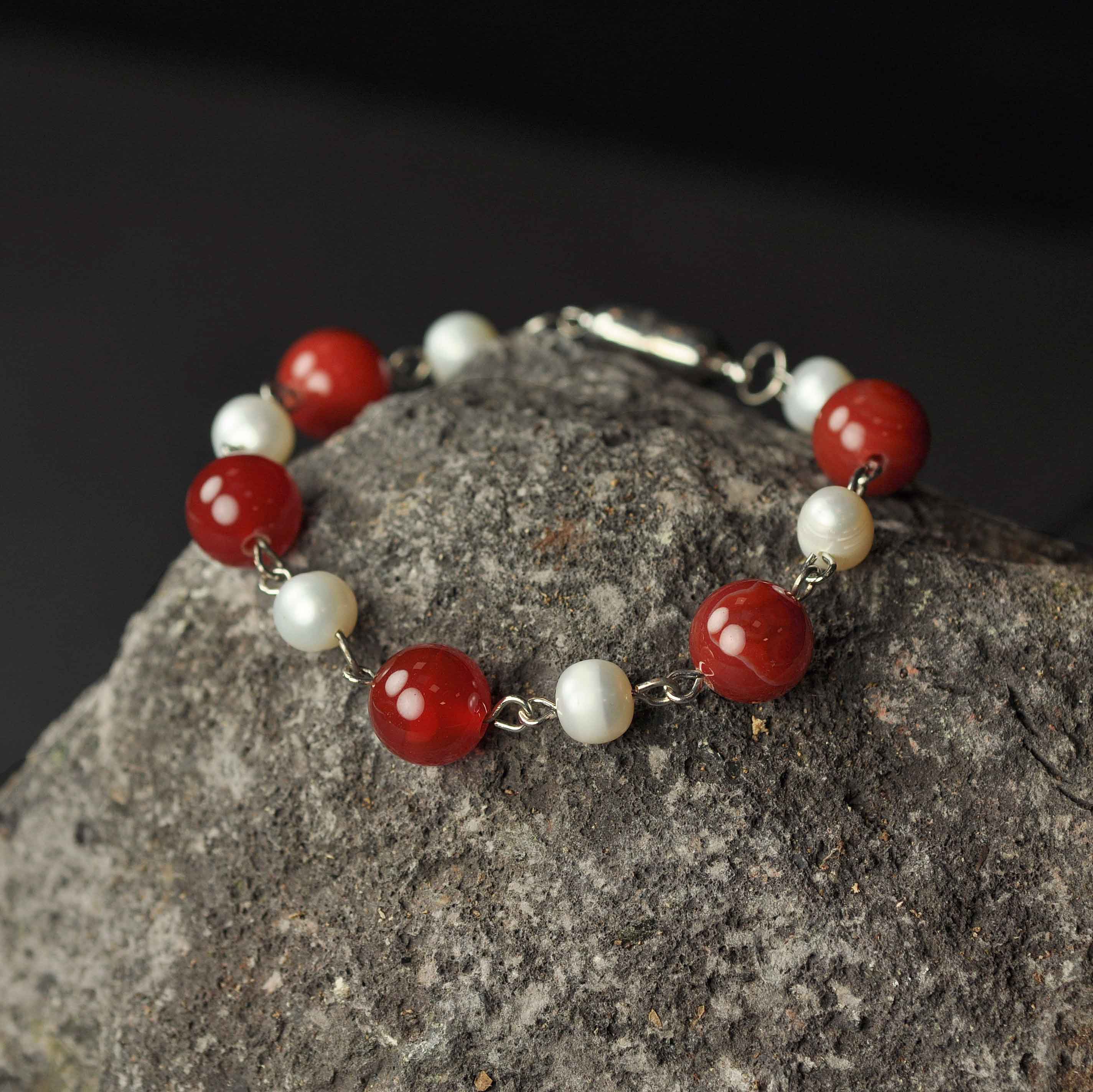 Wit zoetwater parel armband met rode edelstenen (agaat) en magneetslotje liggend op rots - Pearl Red Agate Ball