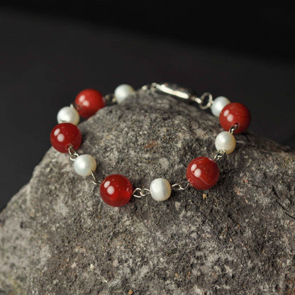 Wit zoetwater parel armband met rode edelstenen (agaat) en magneetslotje liggend op rots - Pearl Red Agate Ball