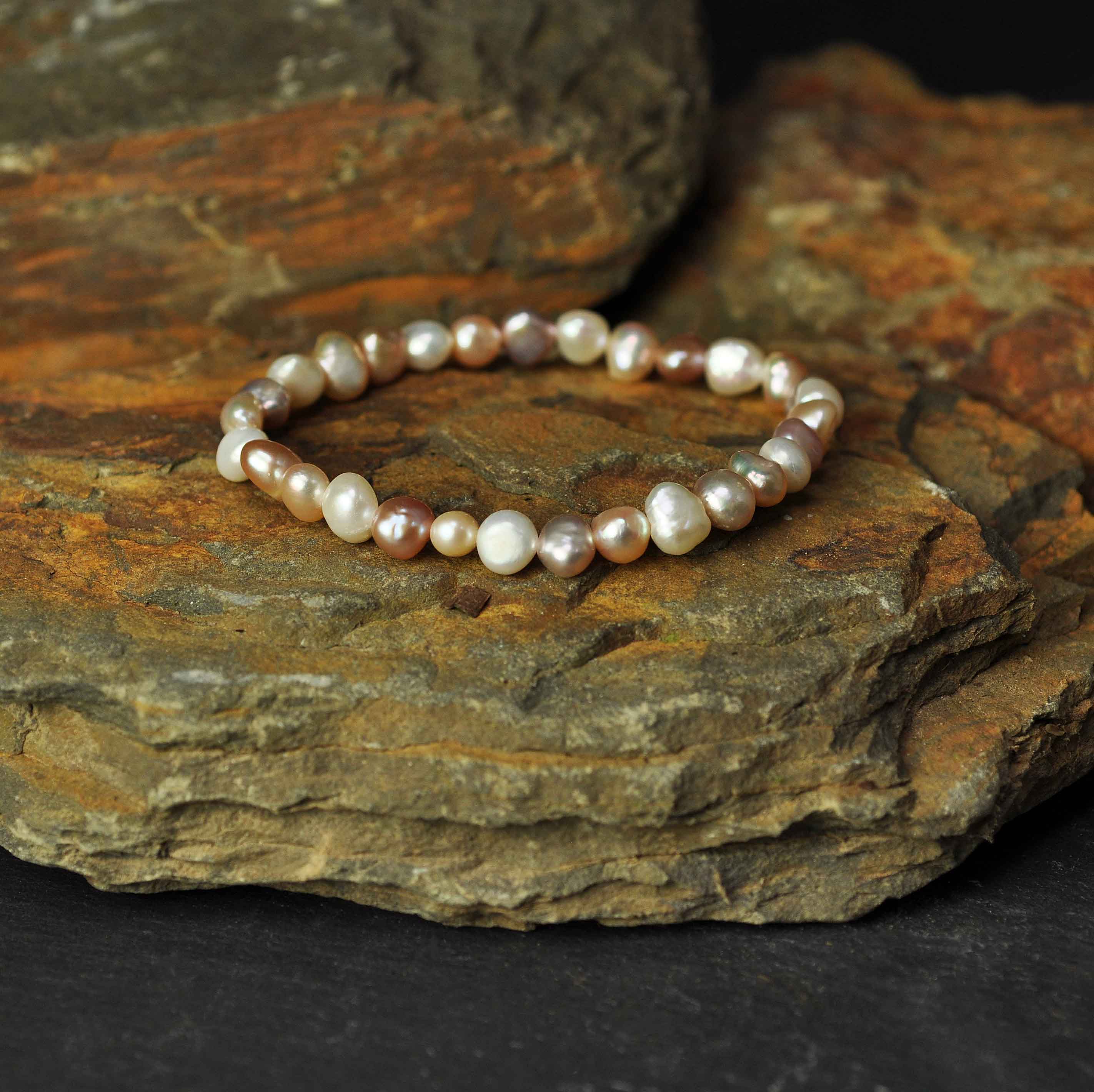 Elastisch zoetwater parel armband met witte, zalm en roze parels liggend op steen | Pearl Soft Colors Pearl Small