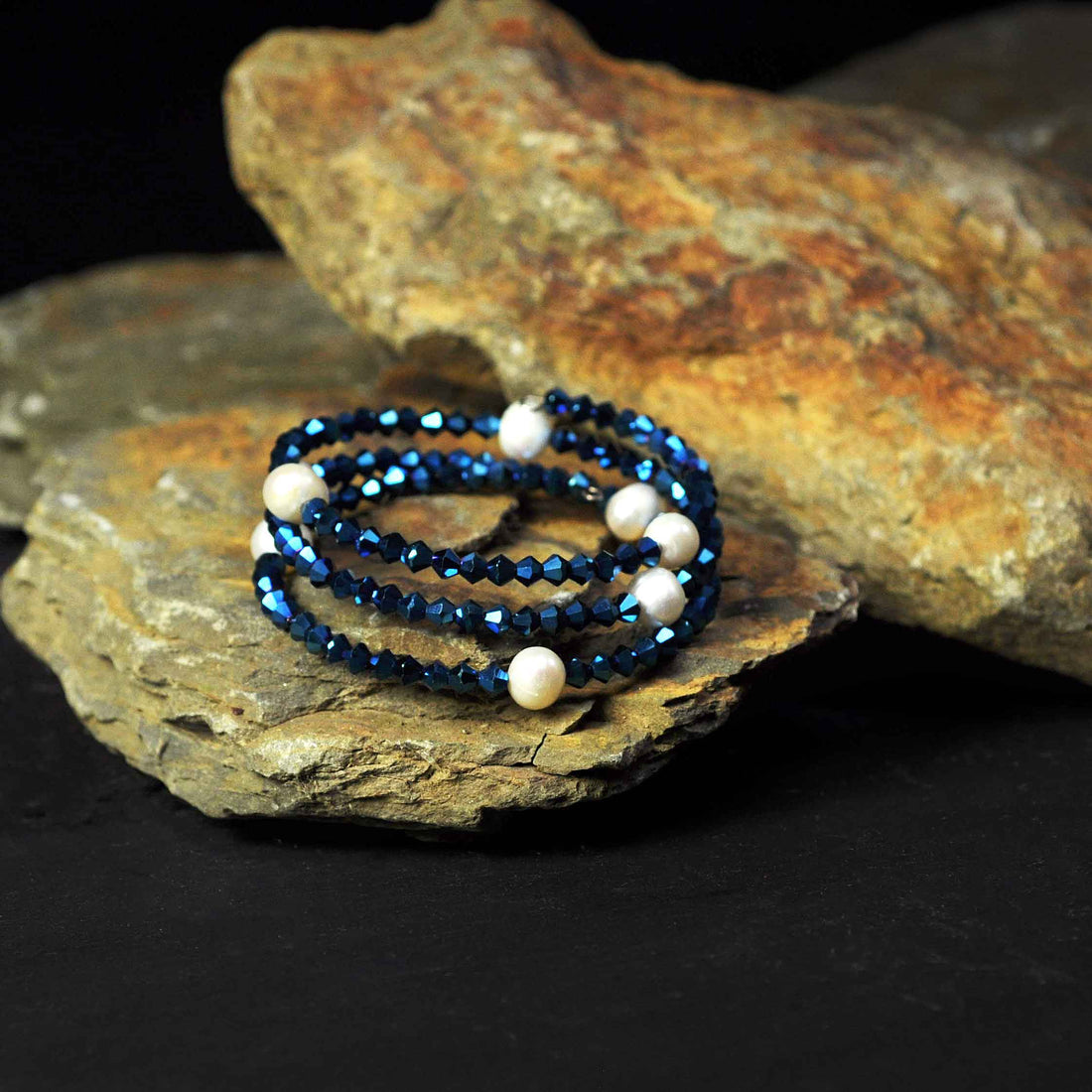 Wit zoetwater parel wikkelarmband met blauwe stras steentjes liggend op steen | Pearl W Metalic Blue
