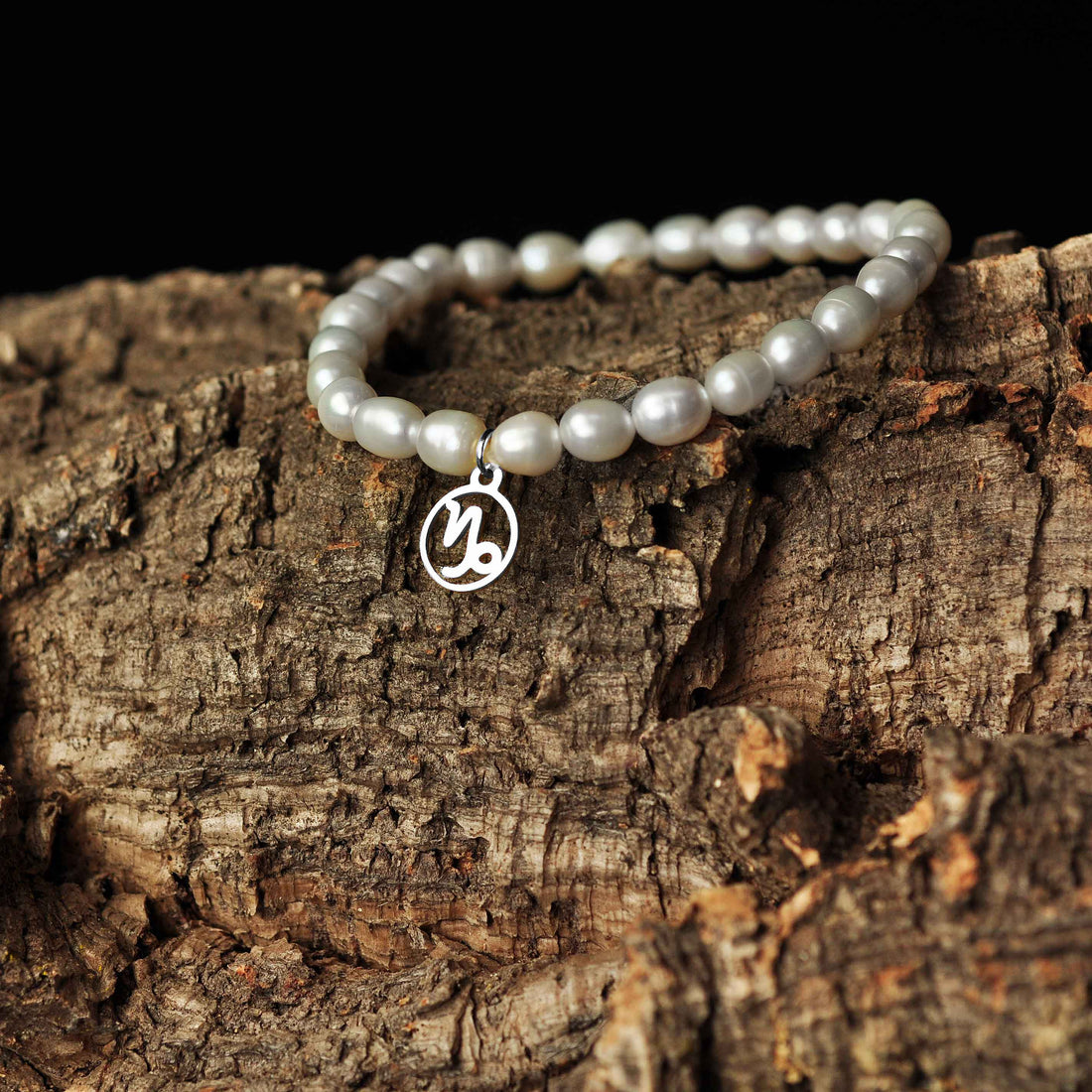 Wit zoetwater parel armband met zilver edelstalen symbool sterrenbeeld steenbok liggend op hout | Parel armband Zilveren Sterrenbeeld Steenbok