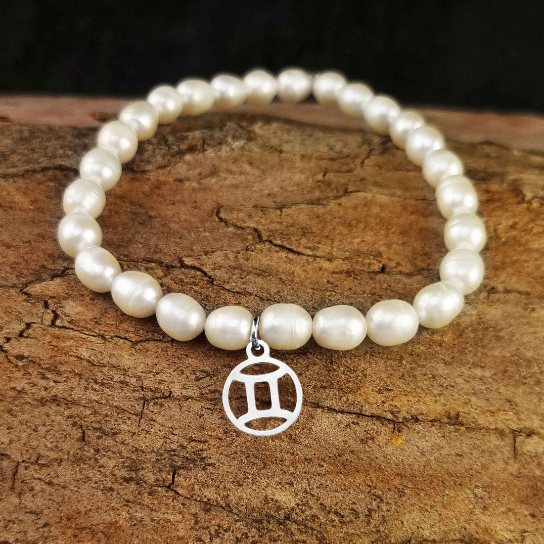 Wit zoetwater parel armband met zilver edelstalen symbool van sterrenbeeld Tweeling liggend op hout | Zilveren Sterrenbeeld Tweeling