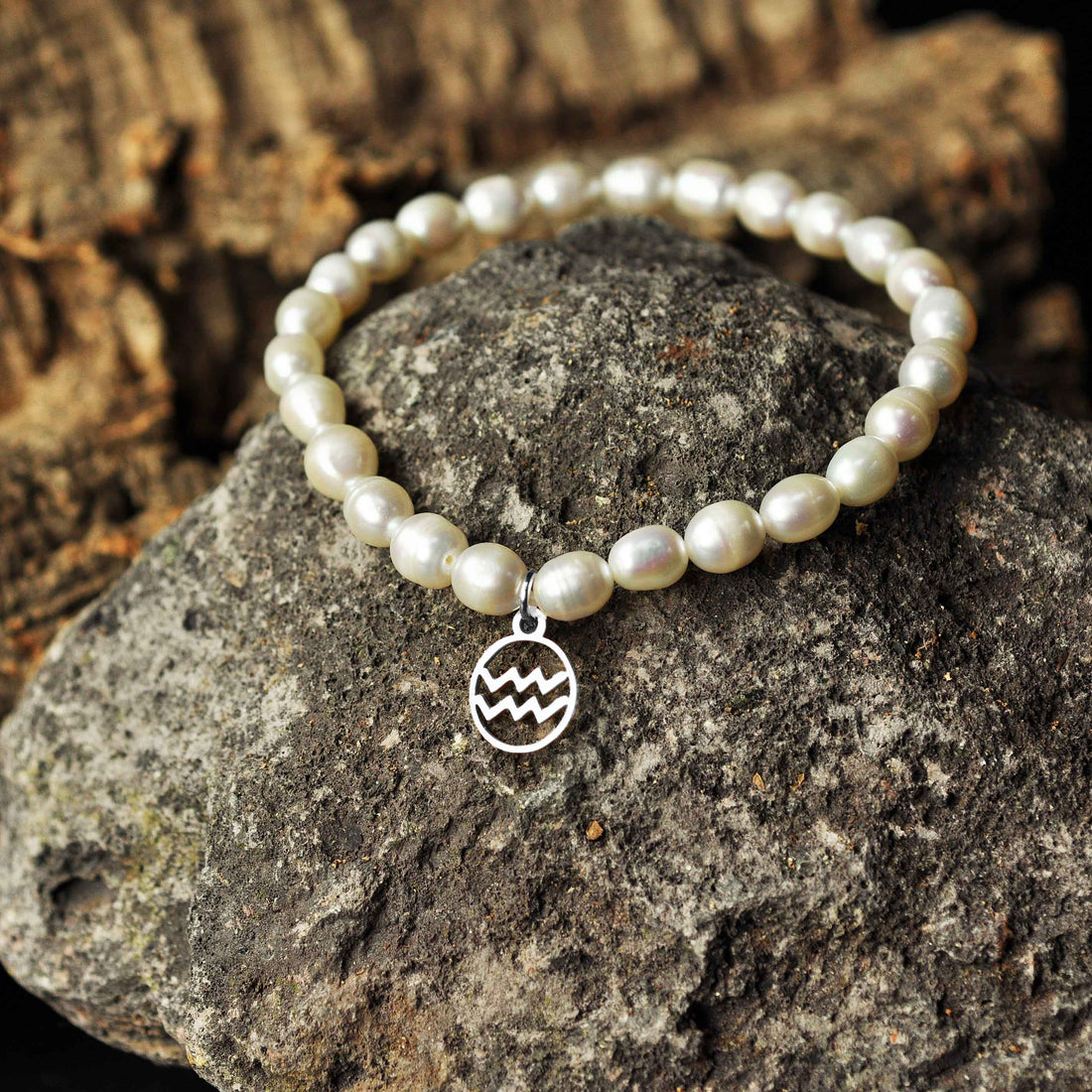 Wit zoetwater parel armband met zilver edelstalen symbool van sterrenbeeld Waterman liggend op zwarte steen | Parel armband Zilveren sterrenbeeld Waterman