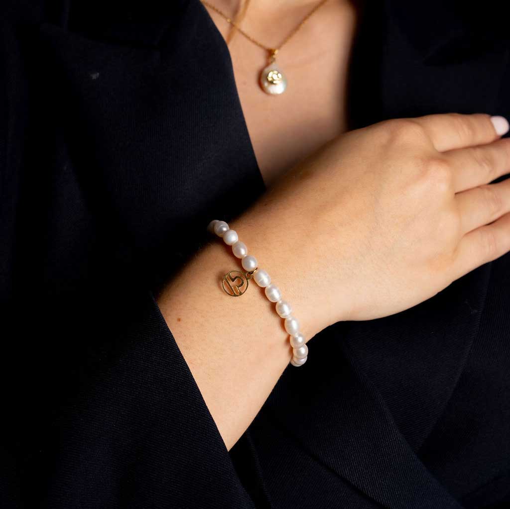 Wit zoetwater parel armband met goud edelstalen symbool van sterrenbeeld Weegschaal op model met colbert | Armband Gouden Sterrenbeeld Weegschaal 