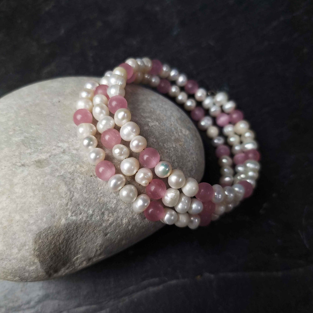 Wit zoetwater parel wikkelarmband met roze edelsteen kattenoog liggend tegen kei | Pearl Pink Cat&