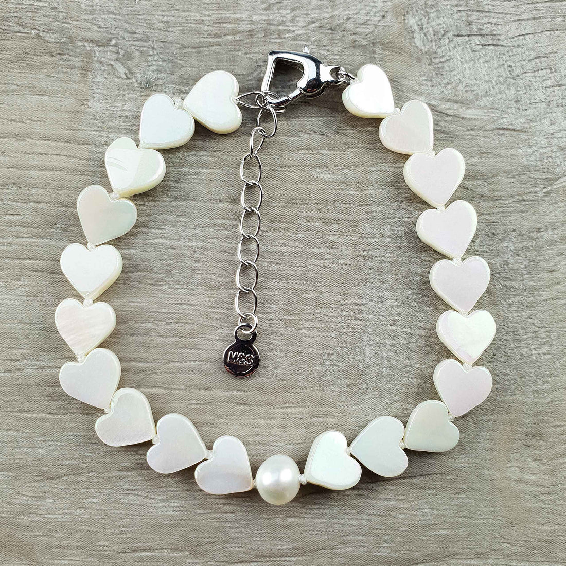 Wit zoetwater parel armband met witte parelmoeren hartjes liggend op houten ondergrond | White Pearl Heart Shell