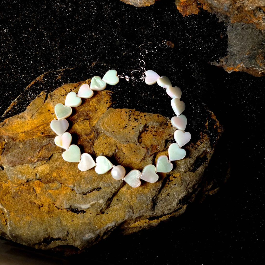 Wit zoetwater parel armband met wit parelmoeren hartjes liggend op zwart zand | White Pearl Heart Shell
