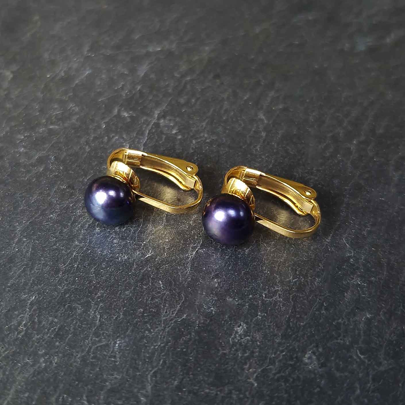 Zoetwater parel clips oorbellen met blauw zwarte parel en goud edelstaal liggend op leisteen | Gold Black Clip Pearl 8 mm
