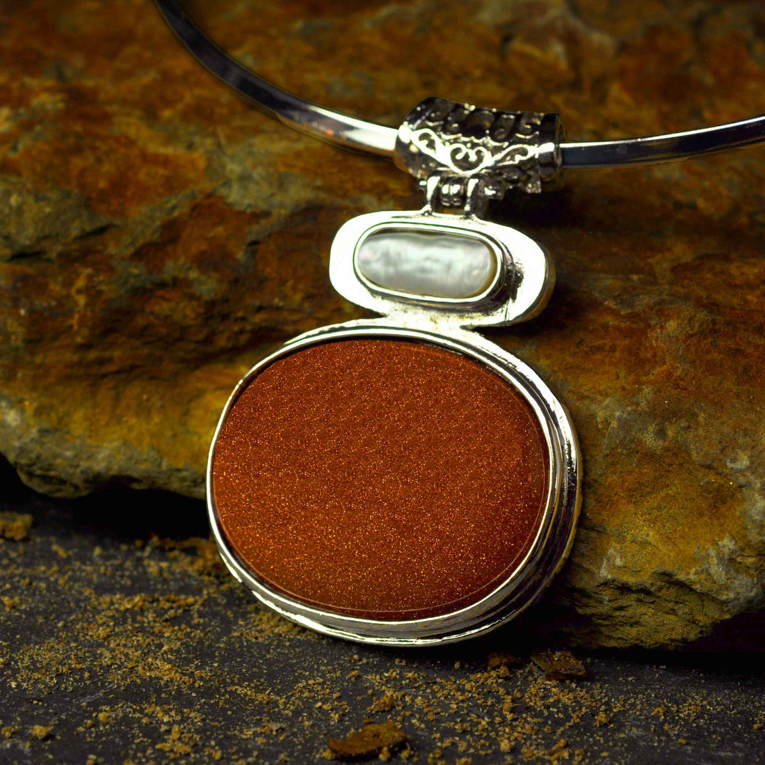 Detail van zoetwater parelketting met bruine edelsteen goudsteen hanger liggend op steen | Biwa Goldsand