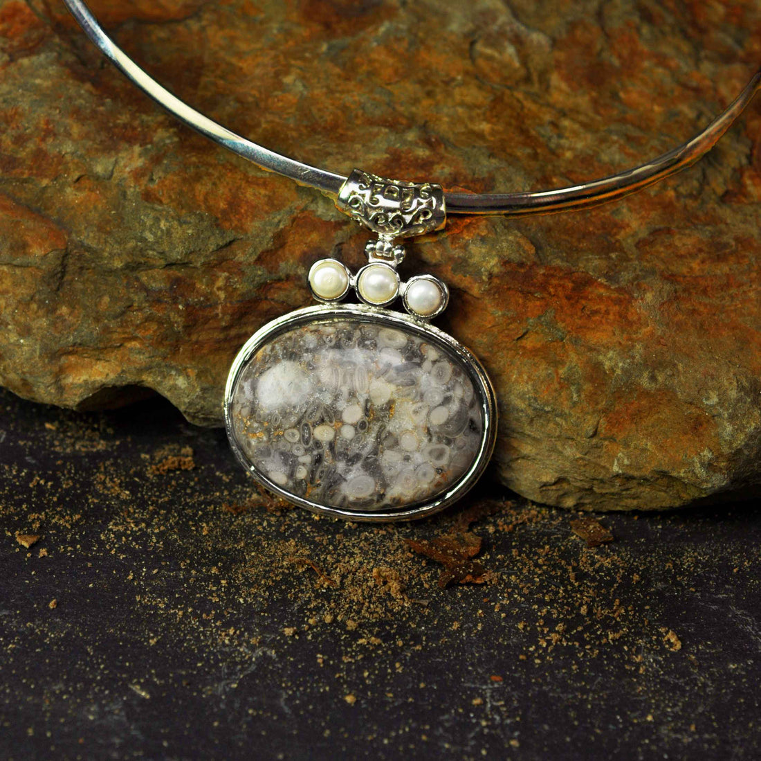 Detail van zoetwater parelketting met grijze edelstenen hanger liggend tegen steen | Three Pearl Grey Gemstone