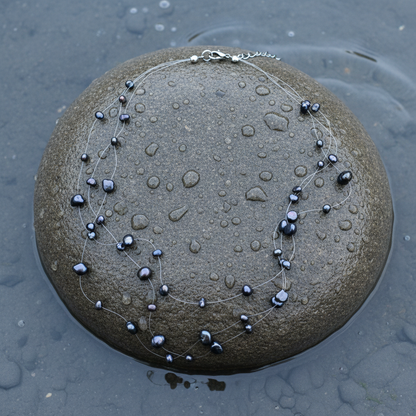 Zoetwater parelketting met zwart blauwe parels in 3 rijen en sterling zilver (925) liggend op natte steen | Jill B
