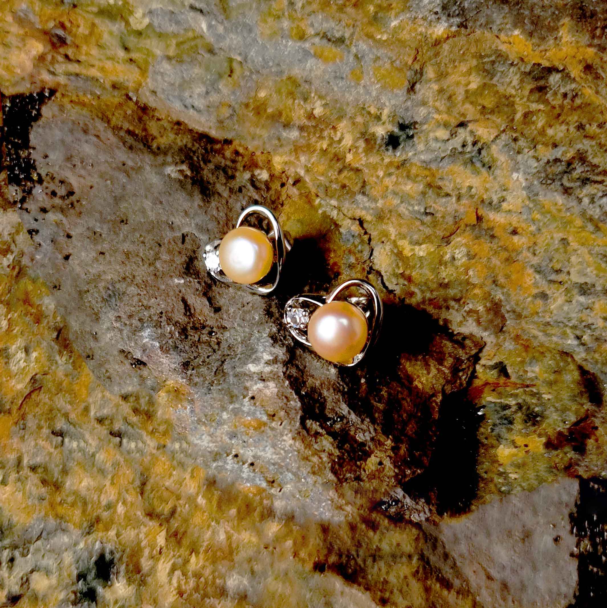 Zalm kleurige oorbellen met zilver hart en stras steentje, oorknop liggend op steen