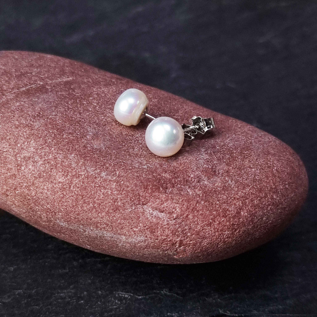 Witte zoetwater parel oorbellen met sterling zilveren oorstekers, witte parel oorknopjes met zilver (925) liggend op rode steen | Mea