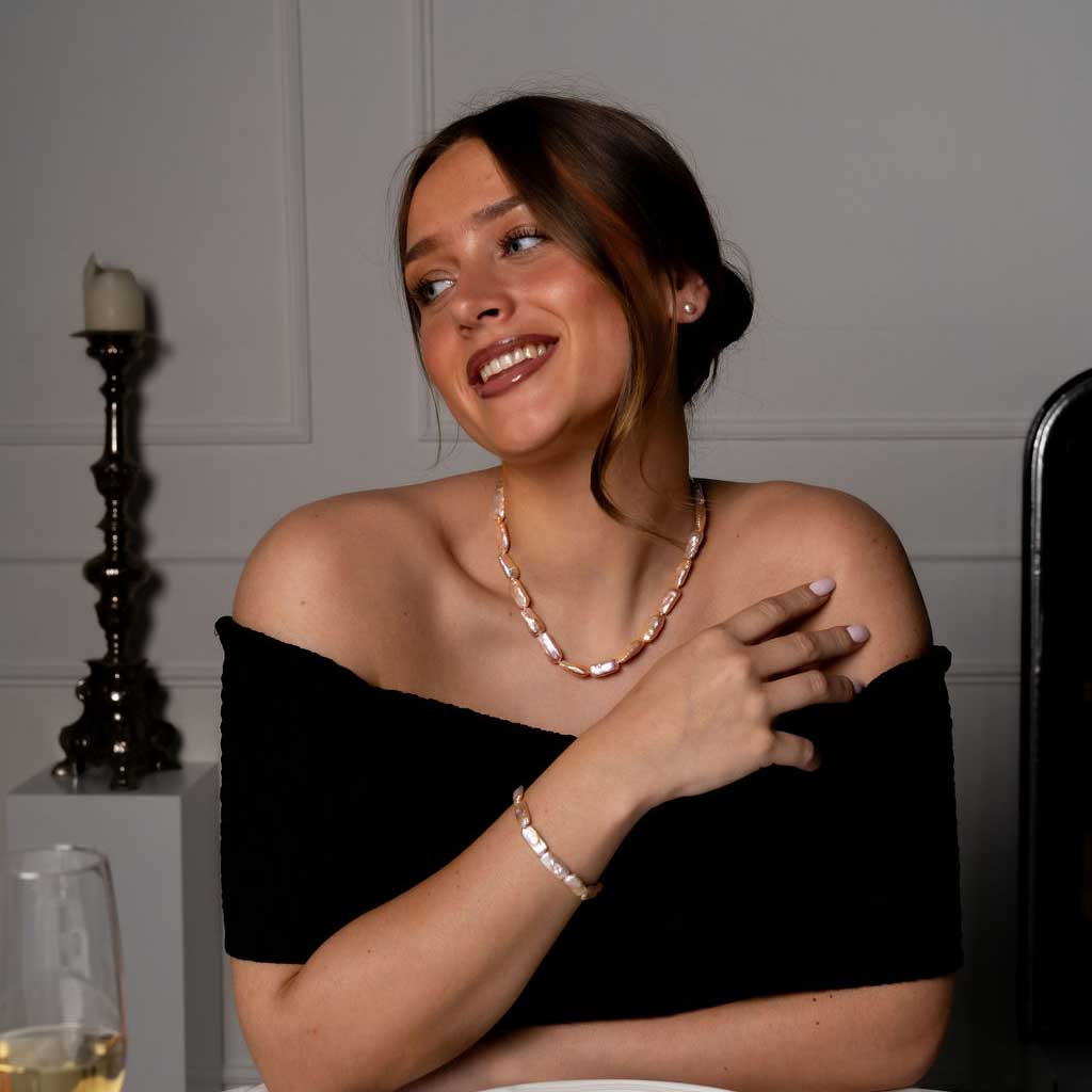 Handgeknoopte zoetwater parel set bestaande uit parelketting en parel armband met zalm kleurige rechthoekige parels en sterling zilver (925) op model aan tafel | set Pearl Rectangle Peach