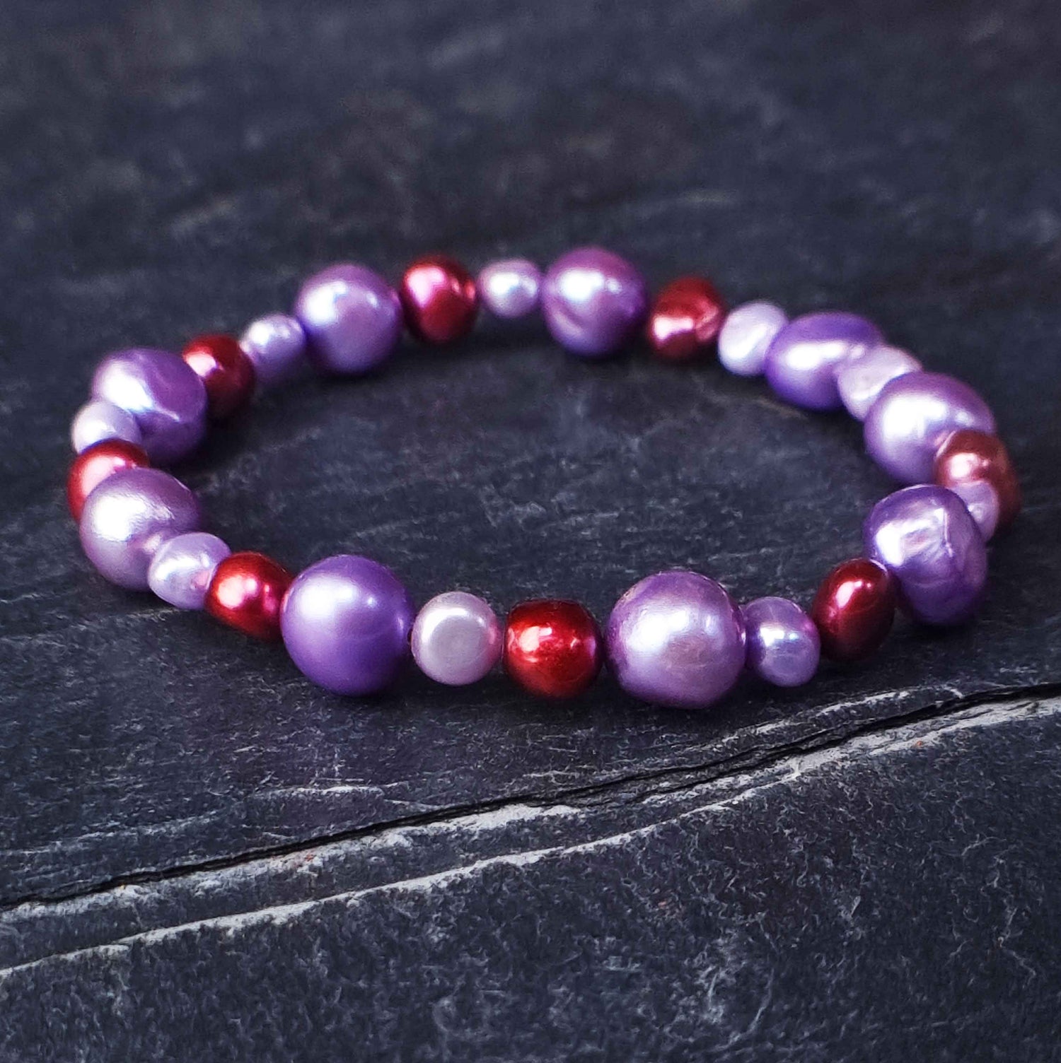 Zoetwater parel armband met lila en rode parels liggend op leisteen | Pulla