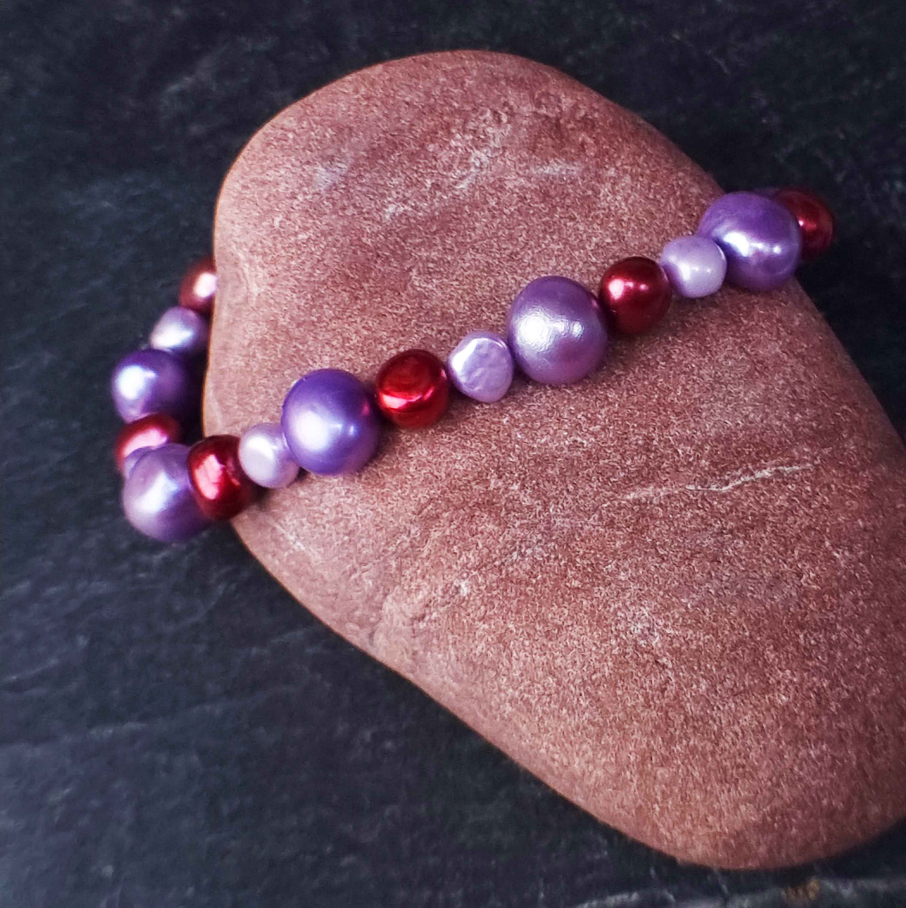 Zoetwater parel armband met lila en rode parels liggend tegen rode steen | Pulla
