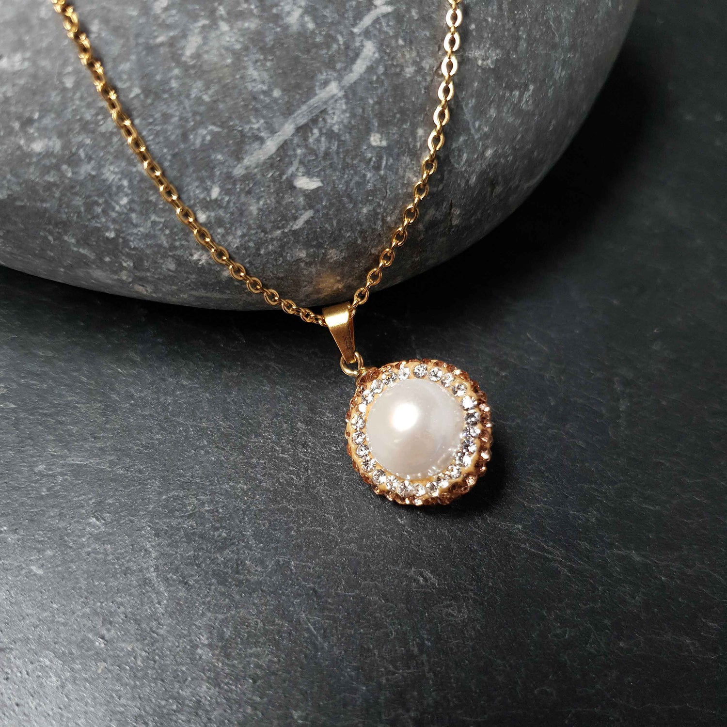 Detail van zoetwater parelketting met witte parel hanger, gouden stras steentjes en goud edelstaal liggend op steen | Bright Golden Pearl