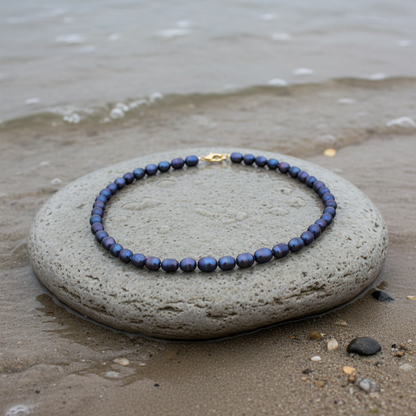 Handgeknoopte zoetwater parelketting met zwarte parels en goud edelstaal liggend op een steen aan de waterrand | Daja