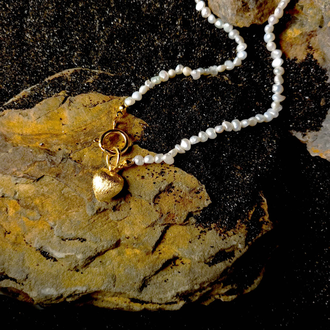 Witte zoetwater parelketting met gouden hart hangertje liggend op zwart zand | Golden Heart Pearl
