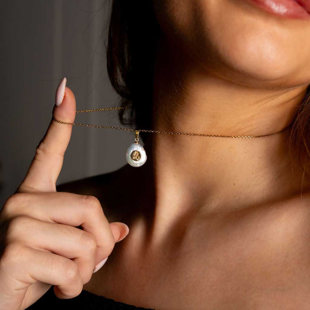 Detail van zoetwater parelketting met witte parel hanger met gouden symbool van sterrenbeeld steenbok en goud edelstaal om hals van model | Gouden Sterrenbeeld Steenbok