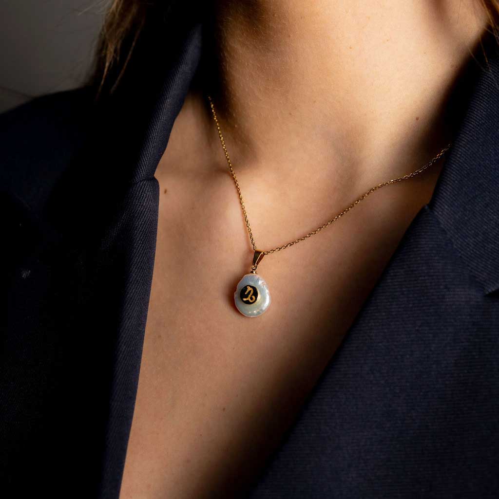 Detail van zoetwater parelketting met witte parel hanger met gouden symbool van sterrenbeeld steenbok en goud edelstaal op model detail | Gouden Sterrenbeeld Steenbok