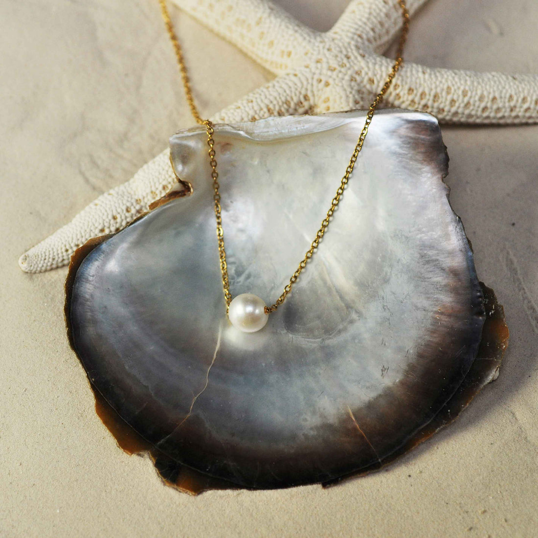 Zoetwater parelketting met witte parel aan goud edelstalen ketting liggend in witte schelp en zand  | Single One Pearl Gold