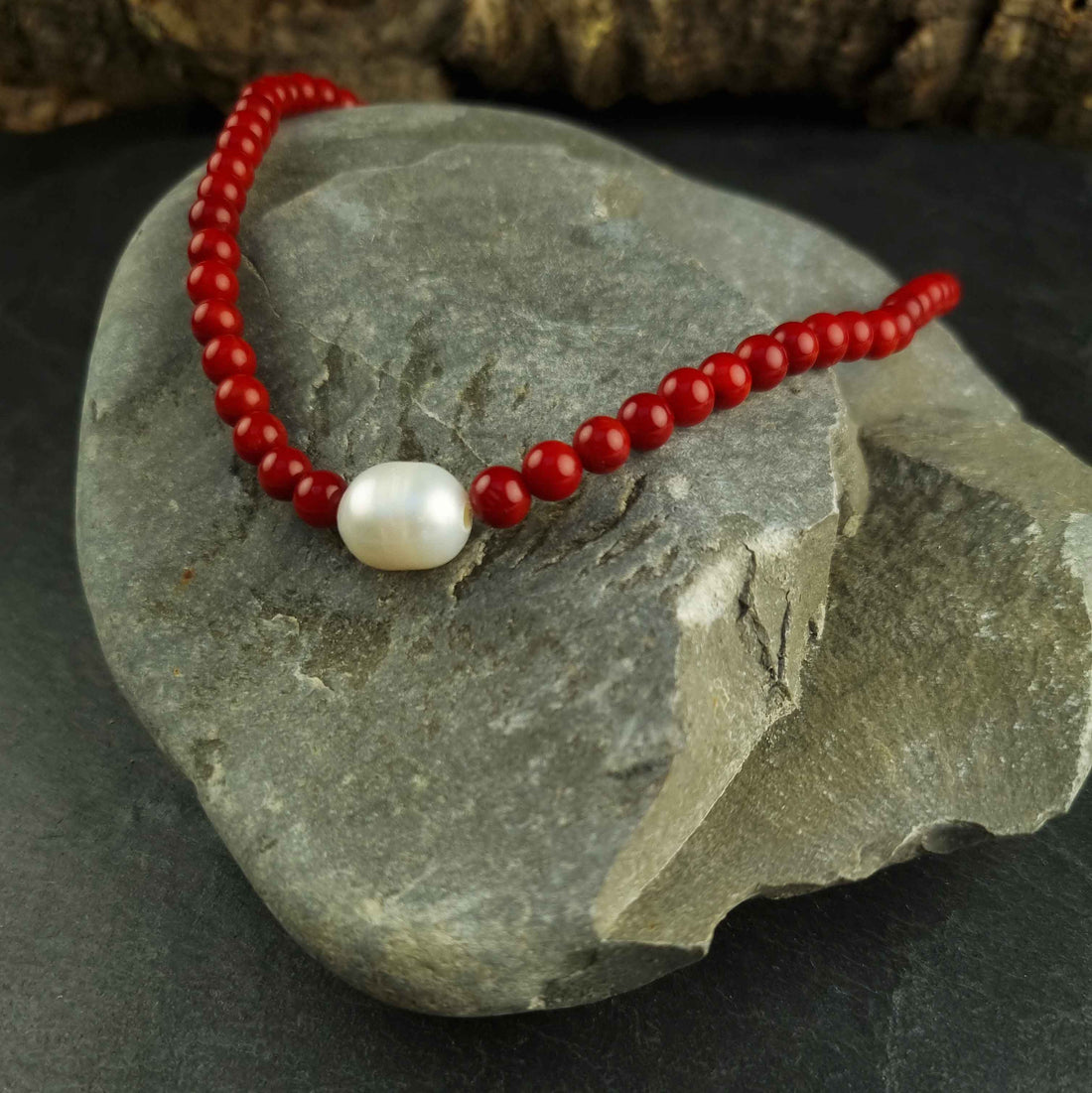 Witte zoetwater parelketting met rood koraal en sterling zilveren slotje liggend op steen | Coral One Pearl W