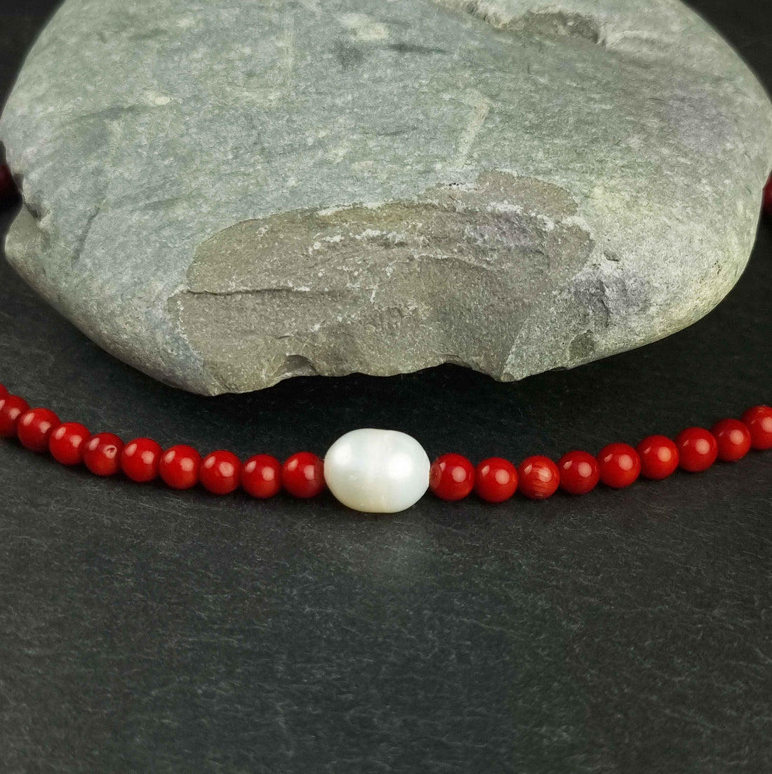 Detail van witte zoetwater parelketting met rood koraal en sterling zilveren slotje liggend op leisteen | Coral One Pearl W