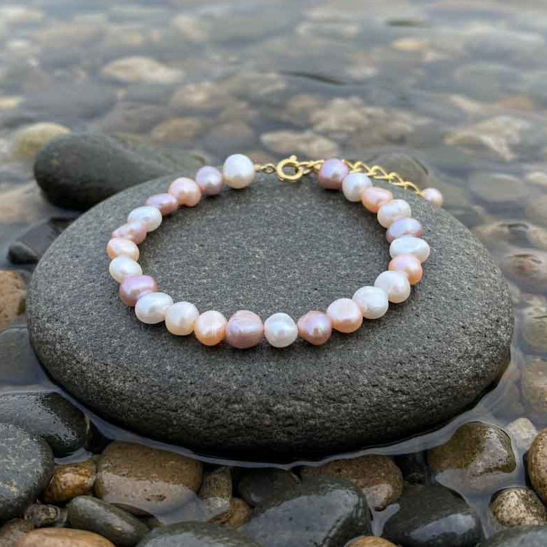 Zoetwater parel armband met witte, roze en zalm kleurige parels met goud edelstaal liggend op steen in water | Aza