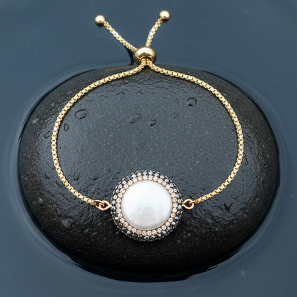 Wit zoetwater parel armband met goud edelstaal, stras steentjes en een schuifslotje liggend op steen in water | Bright Minimal Gold Coin
