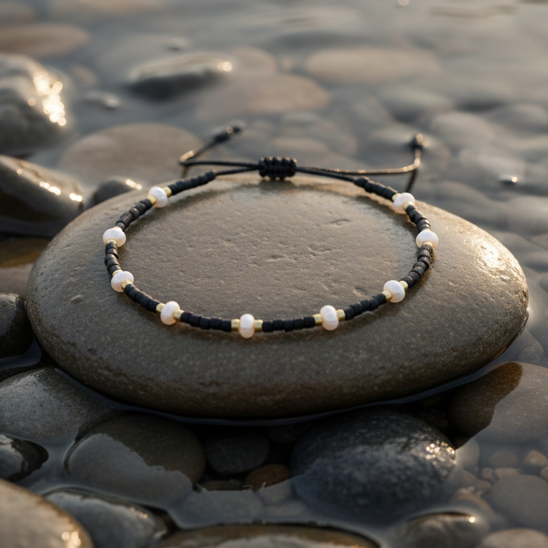 Wit zoetwater parel schuif armband met zwarte en gouden kraaltjes liggend op steen in water | Mini Pearl Bead Black