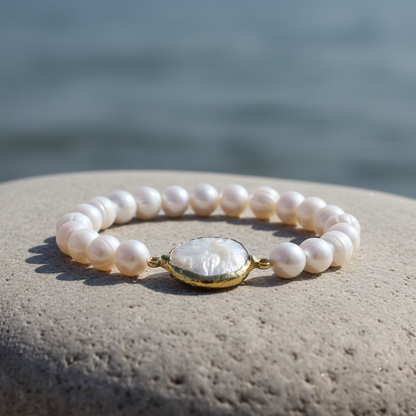 Wit zoetwater parel armband met gouden coin parel liggend op steen bij water, elastisch | One Gold Coin Pearl