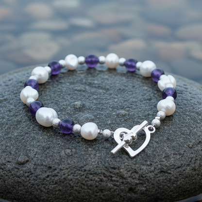Wit zoetwater parel armband met paarse amethist en hartjes slotje liggend op natte steen | Pearl Heart Amethyst