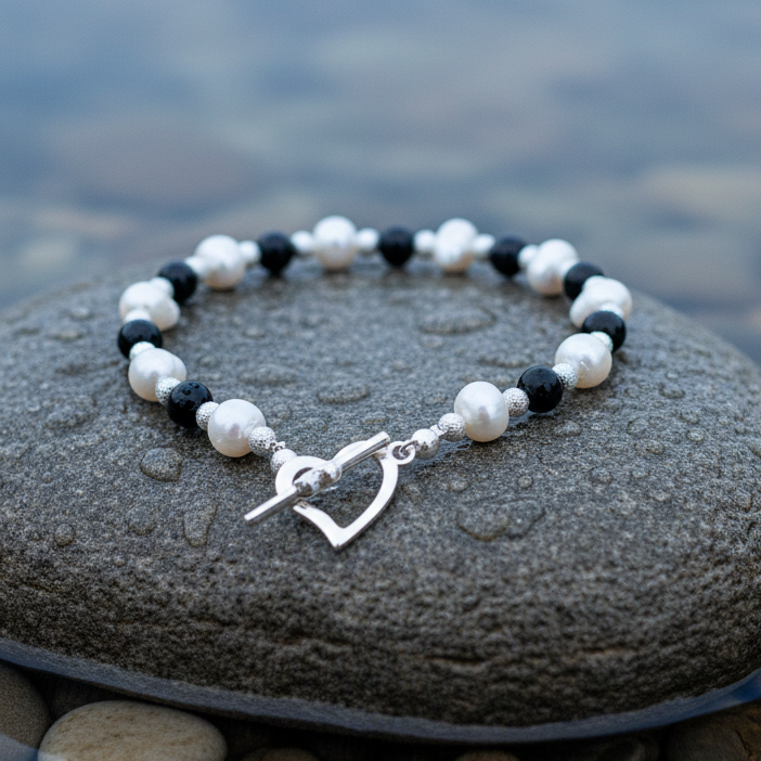 Wit zoetwater parel armband met zwarte agaat en hartjes slotje liggend op natte steen | Pearl Heart Black Agate
