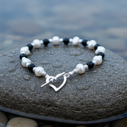 Wit zoetwater parel armband met zwarte agaat en hartjes slotje liggend op natte steen | Pearl Heart Black Agate