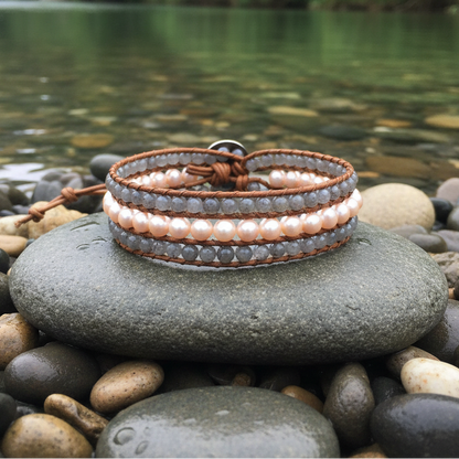 Zoetwater parel armband met zalm kleurige parels, labradoriet en bruin leer liggend op grijze steen in water | Parel armband Kallu
