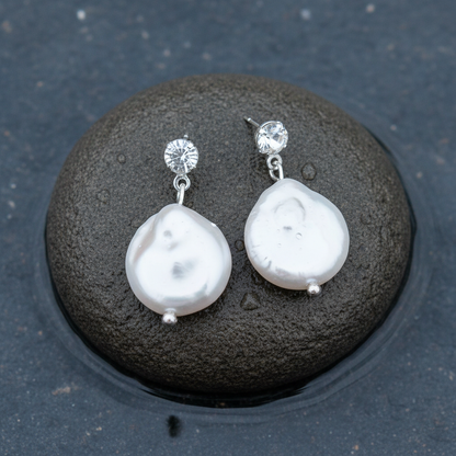 Witte zoetwater parel oorbellen met witte coin parels en stras steentjes liggend op steen in water | Bling Colly