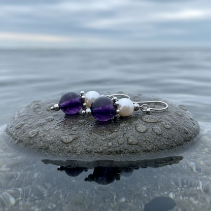 Witte zoetwater parel oorbellen met amethist en sterling zilver (925) liggend op steen | Amilia Amethyst
