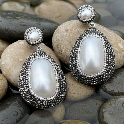 Grote witte zoetwater parel oorbellen met stras steentjes liggend op stenen | Bright Shell Oval