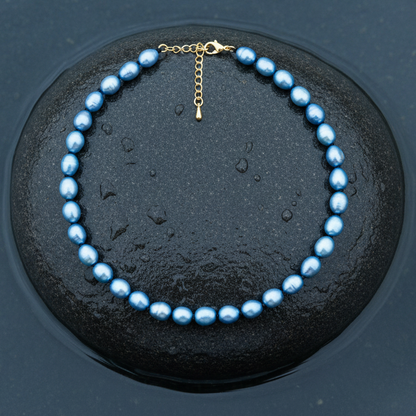Blauw zoetwaterparel ketting met goud edelstalen slotje is volledig handgeknoopt met barok parels en ligt op steen in water | Blair