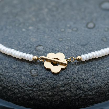 Zoetwater parelketting met kleine witte parels en gouden bloem slotje liggend op steen in water close up | Bloem