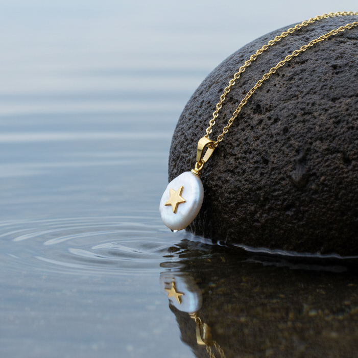 Detail van zoetwater parelketting met witte parel hanger met gouden ster en goud edelstaal liggend op steen | Coin Pearl Golden Star 