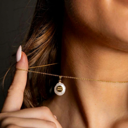 Detail van witte zoetwater parelketting met hanger en symbool van sterrenbeeld Waterman en goud edelstaalop model close up | Gouden Sterrenbeeld Waterman