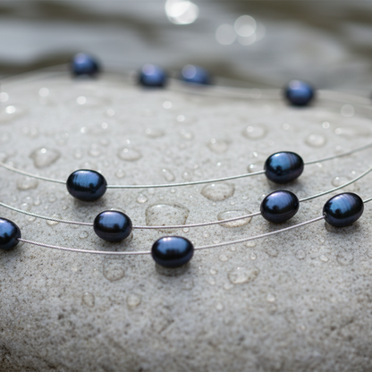 Zoetwater parelketting met blauw zwarte parels in 3 rijen liggend op steen in water close up | Jill Black