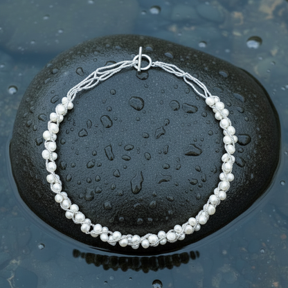 Witte zoetwater parelketting liggend op steen in water | Monica